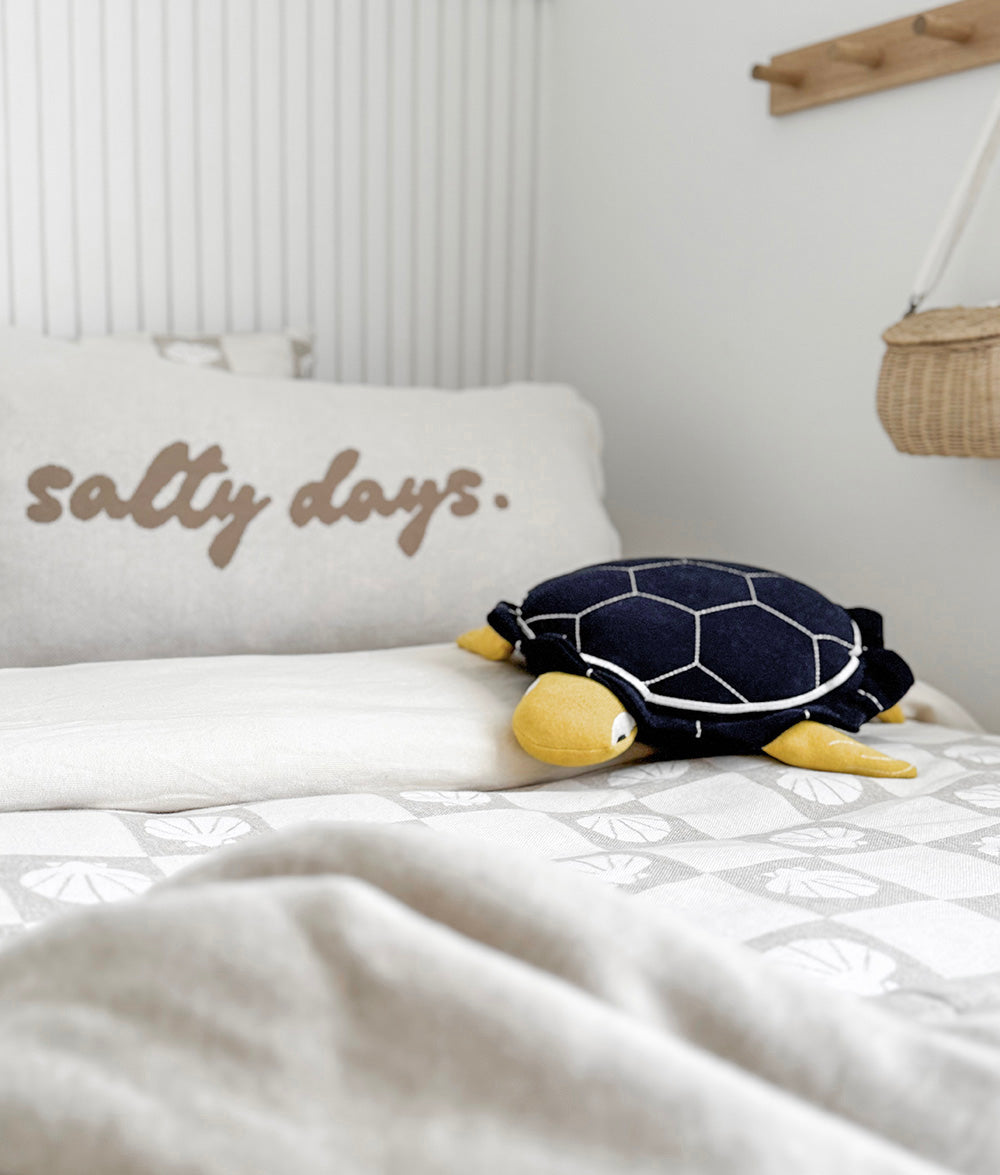 Turtle plush toy on a bed with 'salty days' pillow