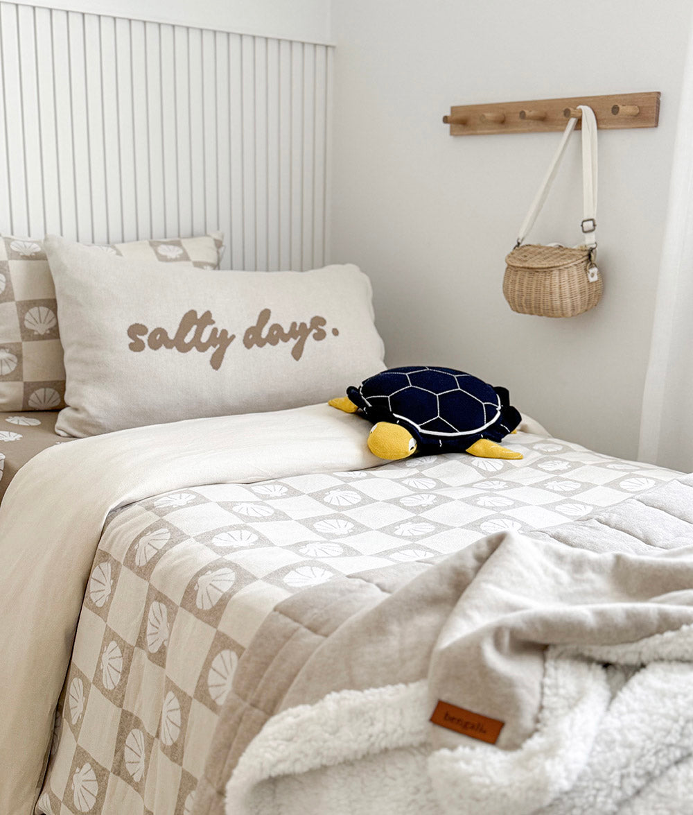 Bedroom with a bed featuring a pillow with 'salty days' text, a turtle plush toy, and a blanket.
