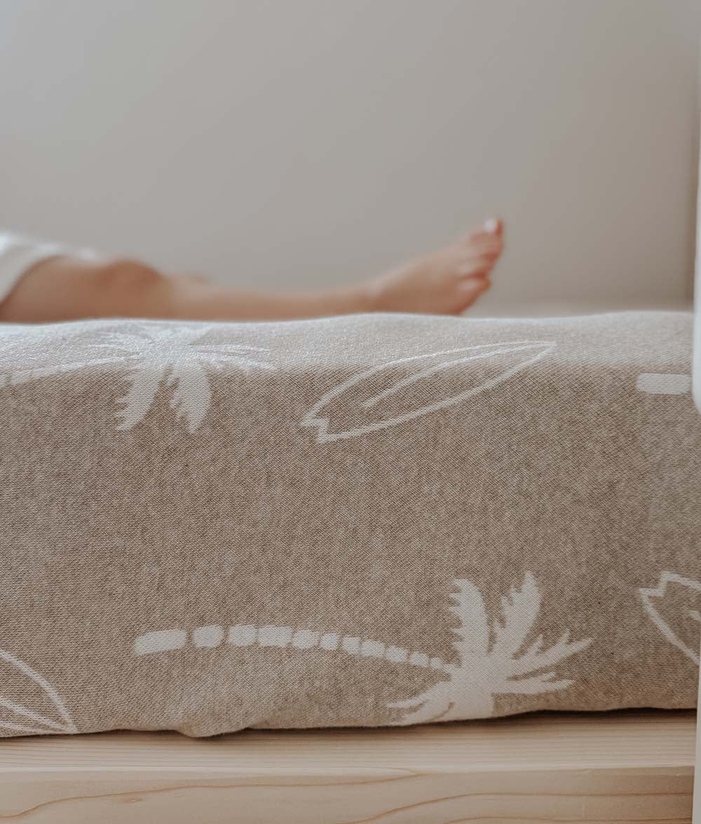 Close-up of a beige fabric with white floral patterns on a wooden bed.