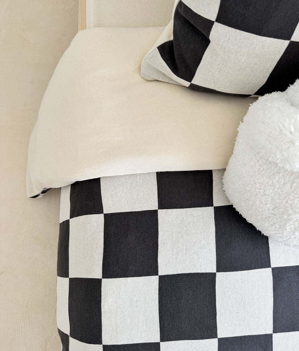Checkered blanket draped over a bed with a plush toy on a neutral background