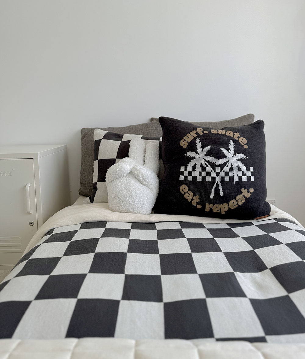 Bed with checkered bedding, decorative pillows, and a white cabinet in the background.