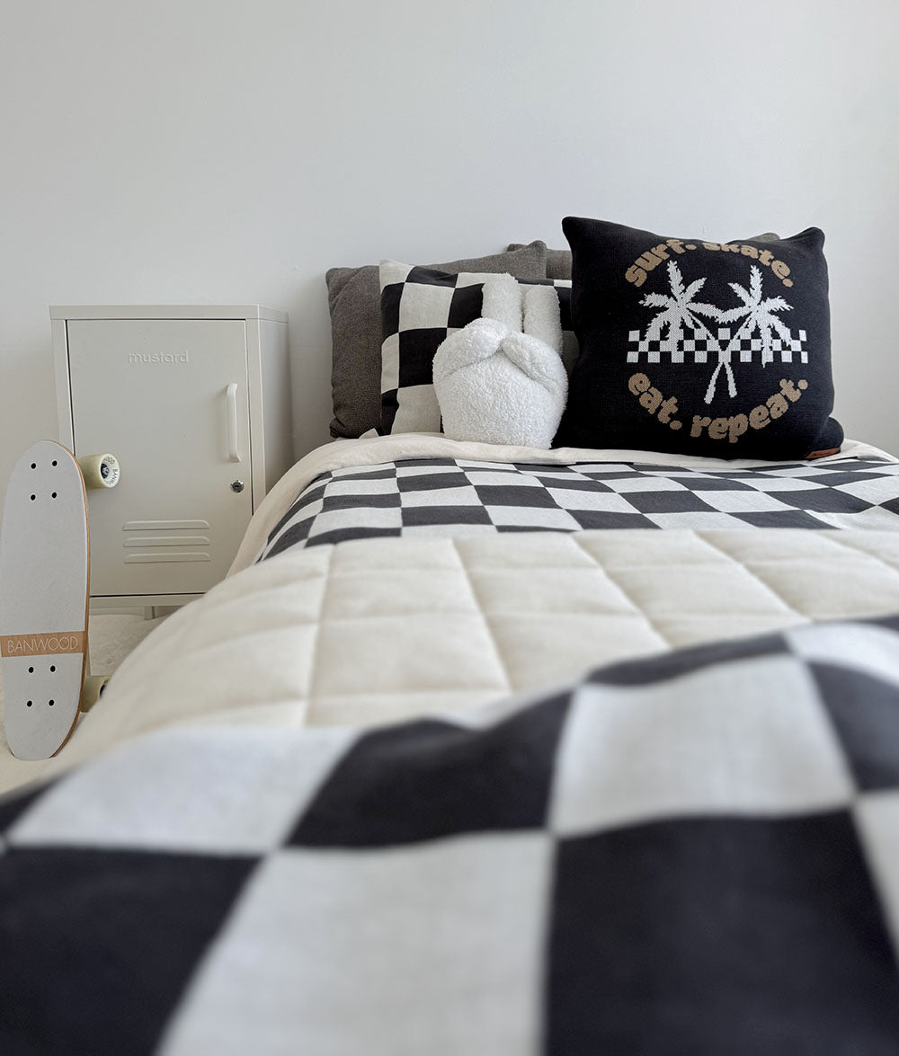 Bed with checkered bedding and decorative pillows in a room with a white locker and skateboard.