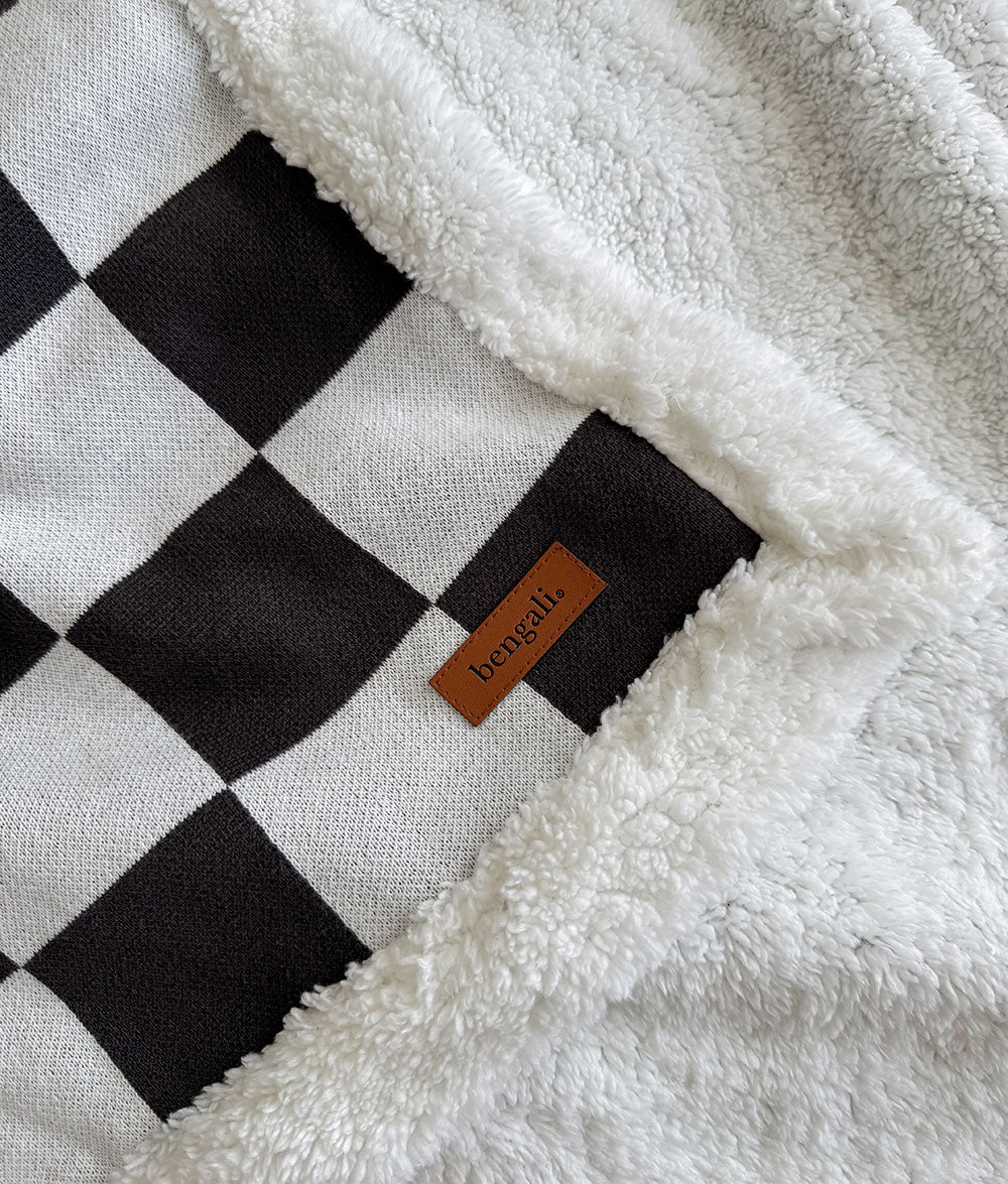 Black and white checkered blanket with a brand label on a soft texture background
