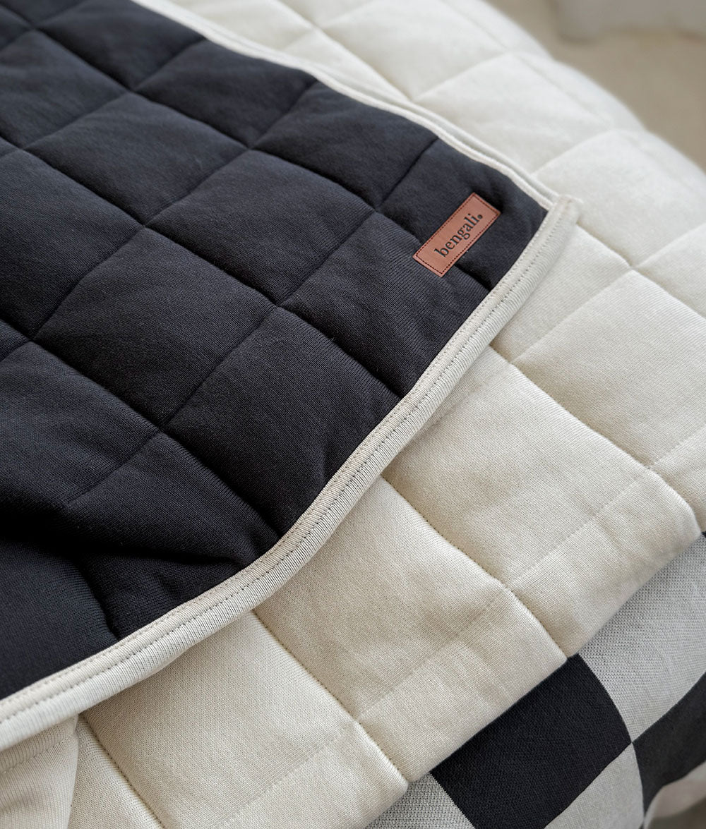 Close-up of a quilted black and beige blanket with a brand label.