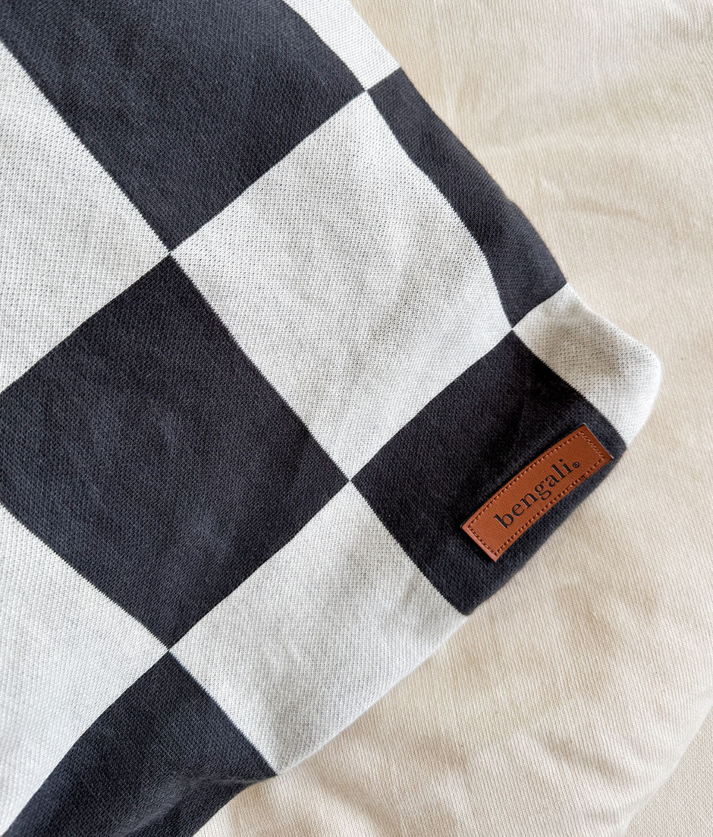 Black and white checkered blanket with a brand label on a beige surface