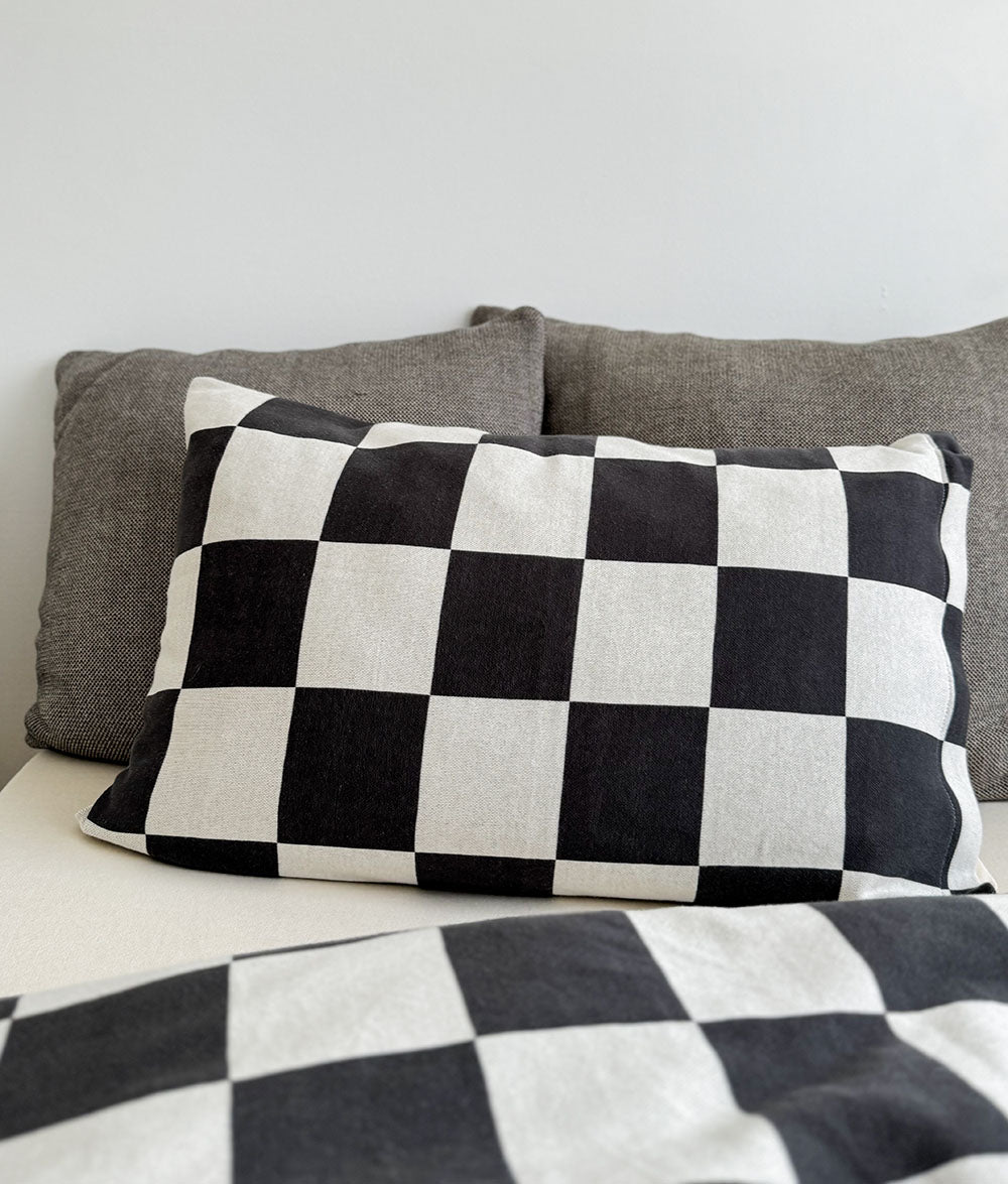 Checkered black and white pillow on a bed with gray cushions.