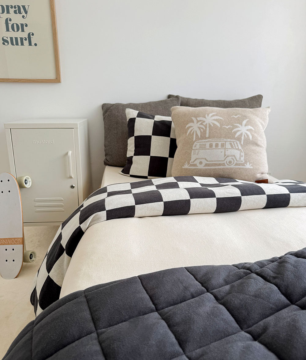 Bedroom with a bed featuring checkered and patterned pillows, a gray comforter, and a white bedside.