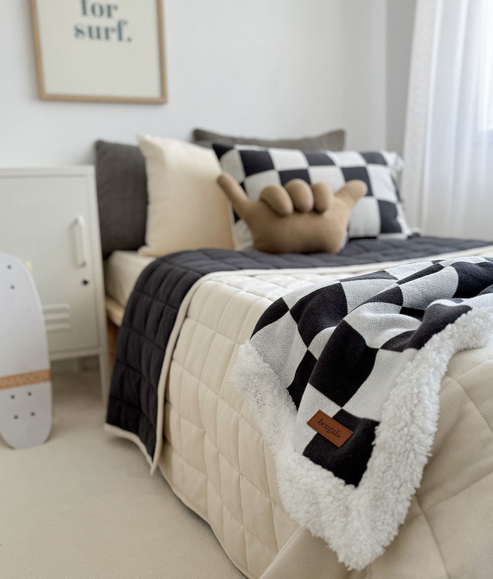 Beige bed with a black and white checkered blanket in a room setting.