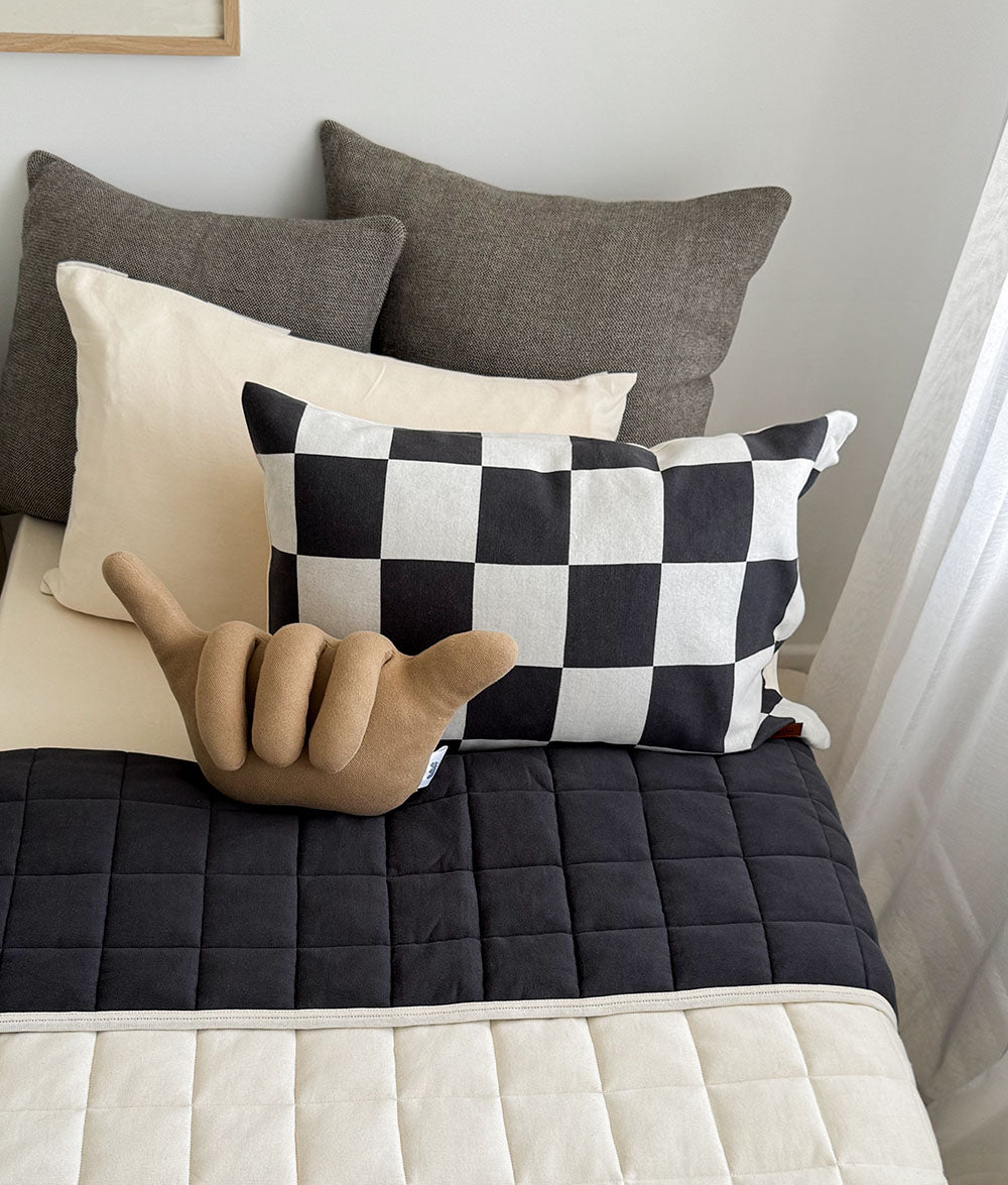 Checkered pillow on a bed with other pillows and a hand gesture model.
