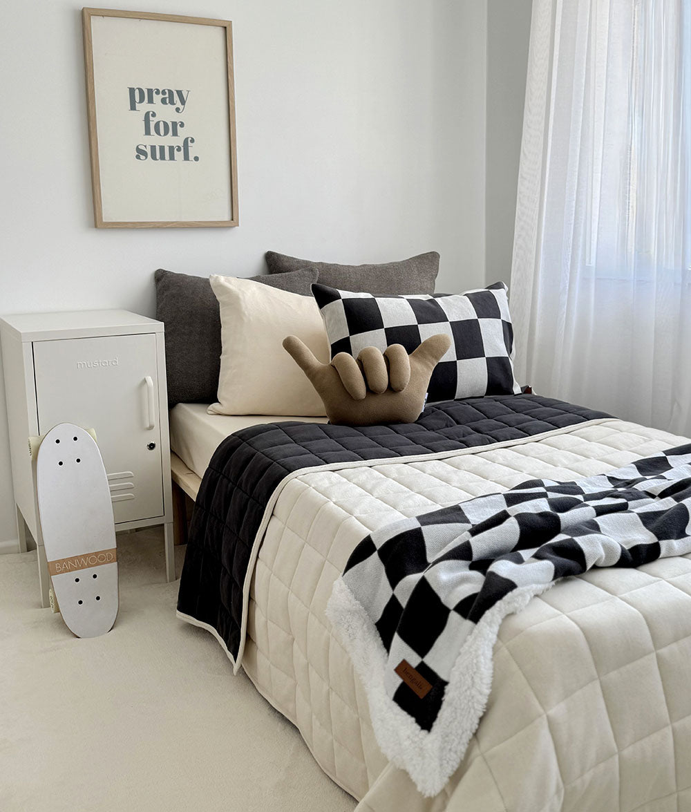 Bedroom with a bed featuring a black and white checkered blanket, pillows, and a skateboard on the floor.