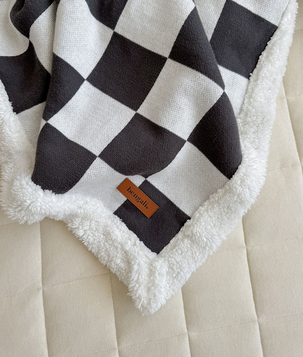 Black and white checkered blanket with a brand tag on a beige surface