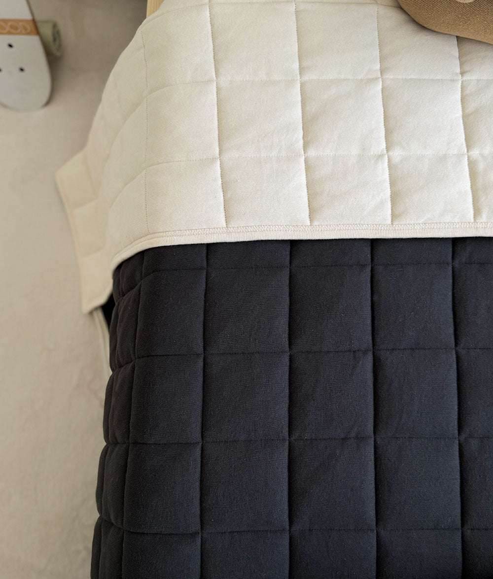 Close-up of a quilted mattress cover with beige top and dark gray bottom.