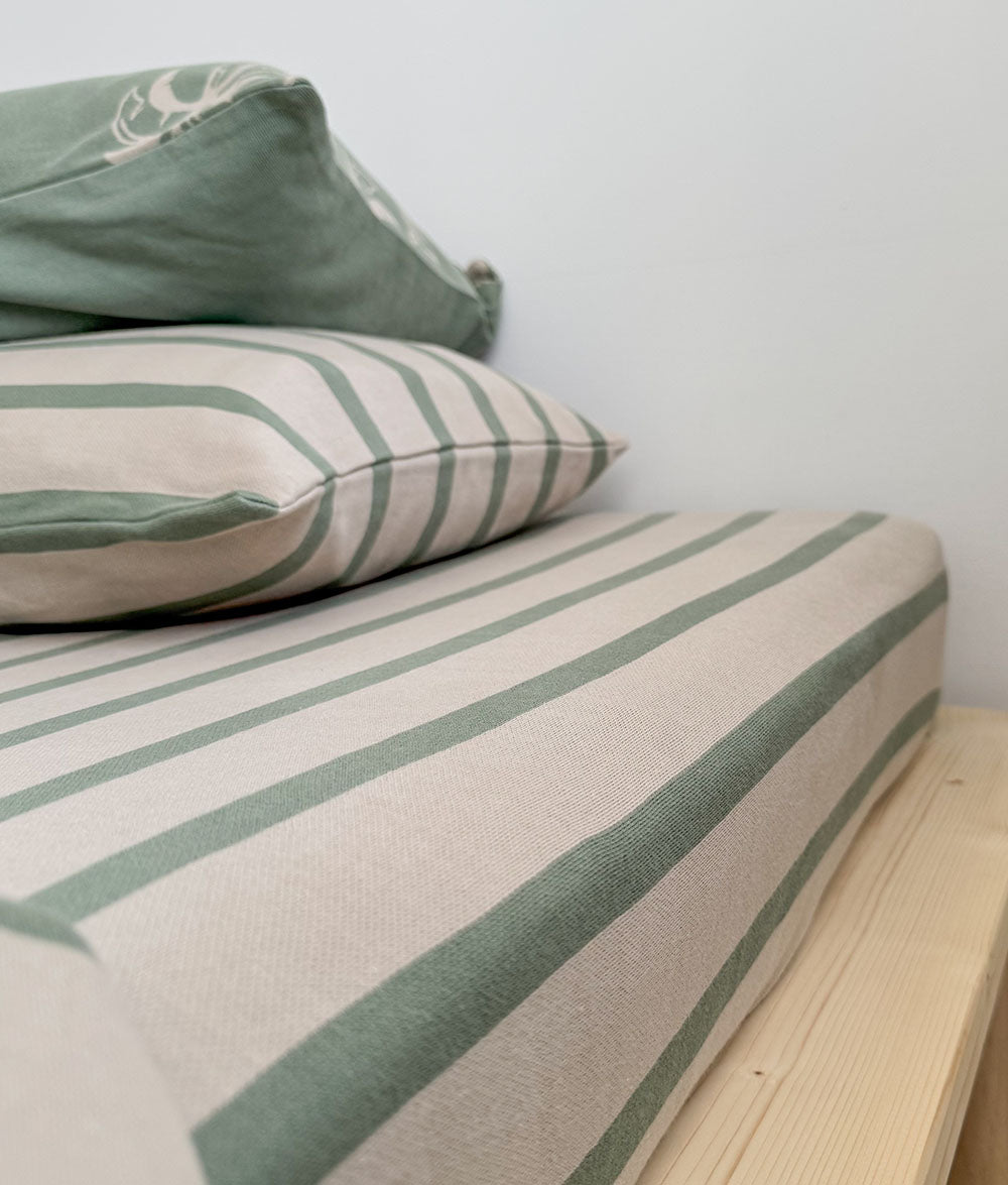 Striped mattress cover with green and beige pattern on a bed against a white wall.