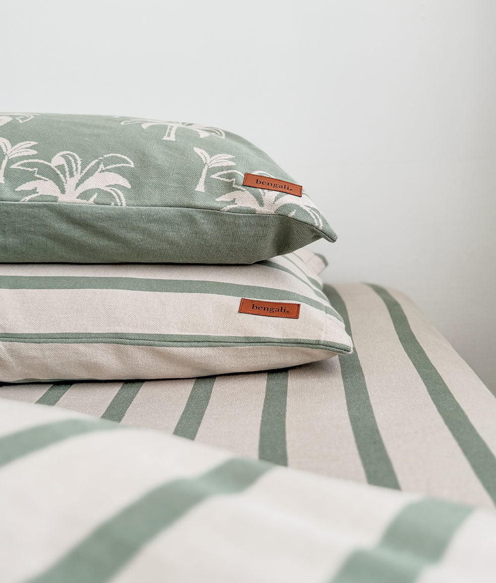 Green and white striped bedding with floral patterned pillows on a bed.