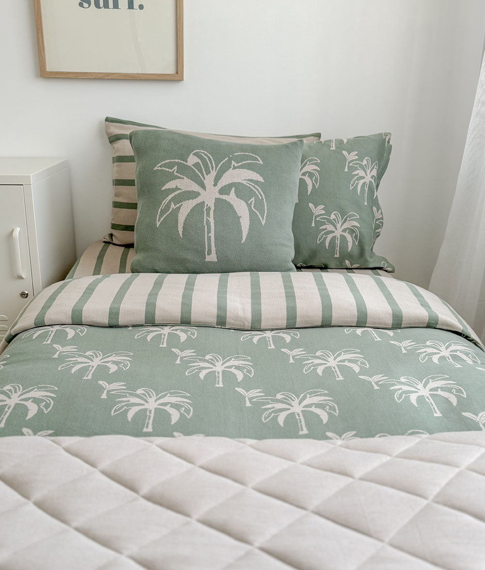 Bed with green and white palm tree patterned bedding and pillows.