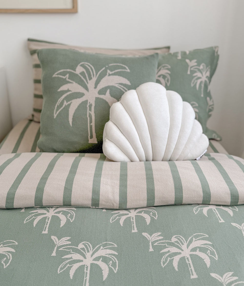 Bed with green and beige striped bedding and palm tree pattern, featuring a shell-shaped decorative pillow.