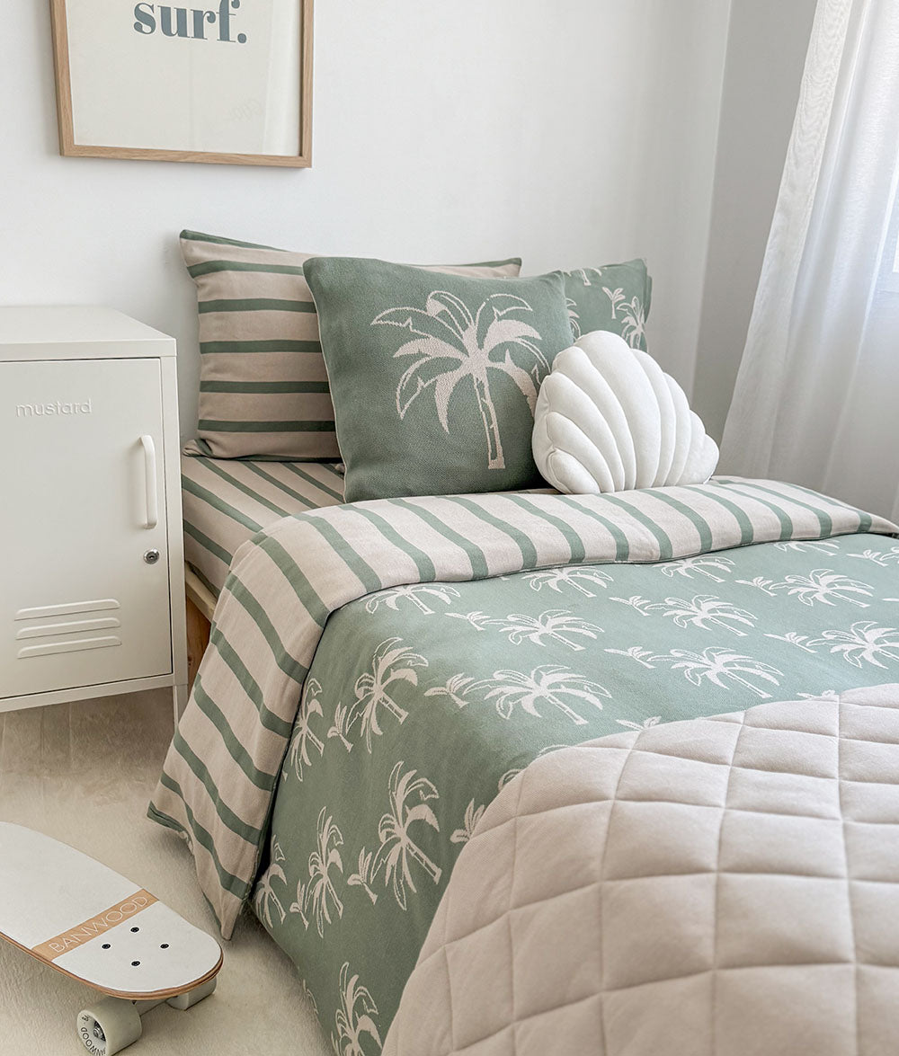 Bed with green and beige striped bedding and palm tree patterns, skateboard on floor.