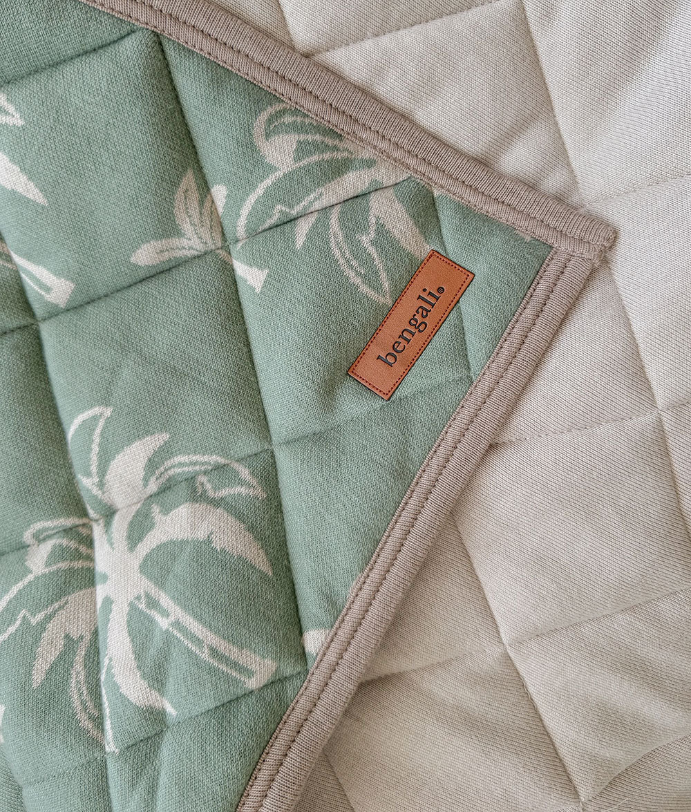 Green fabric with palm tree pattern and 'bengal' brand label on a beige quilted surface.
