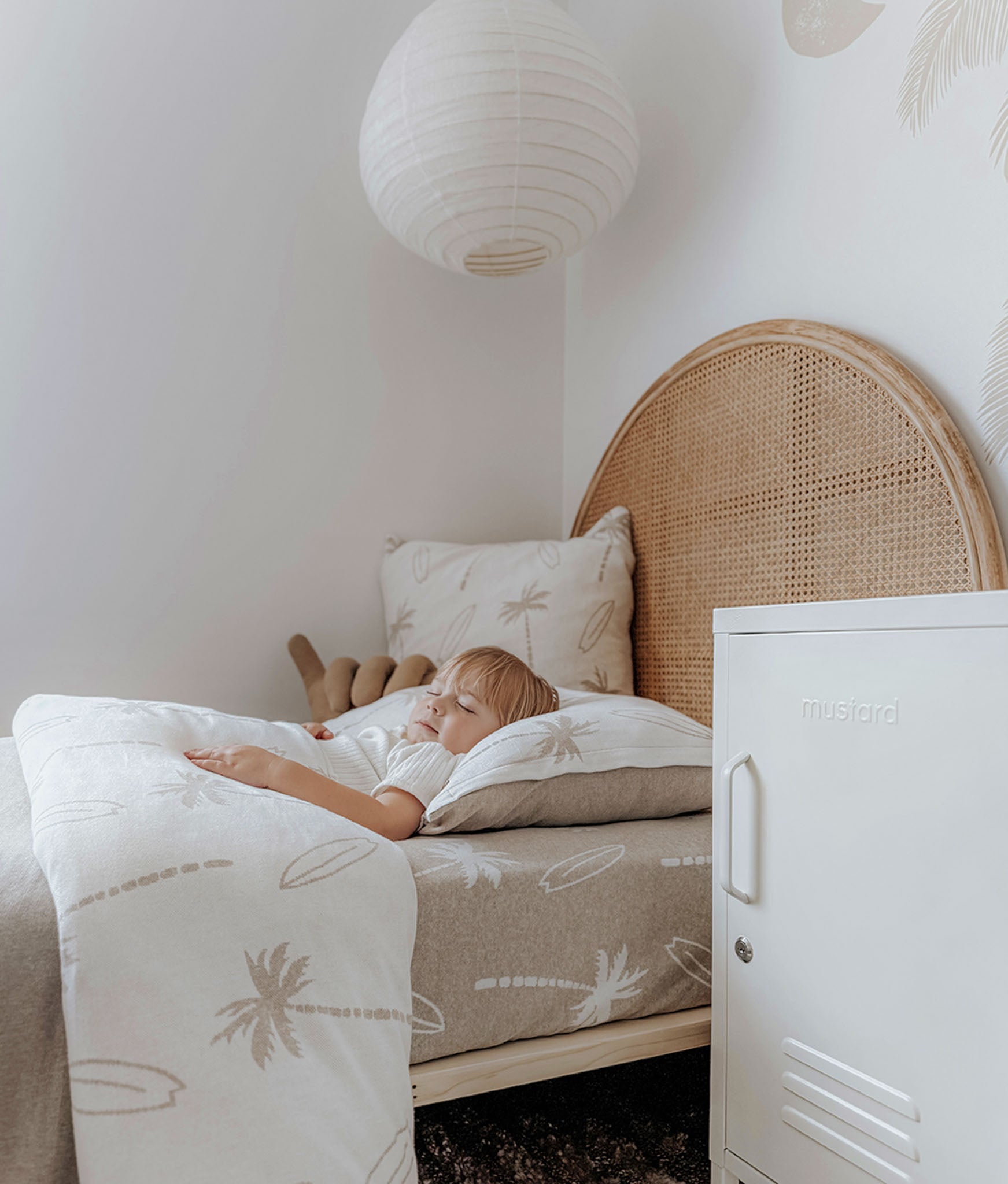 Child sleeping on a bed with a wicker headboard in a room with a white cabinet.