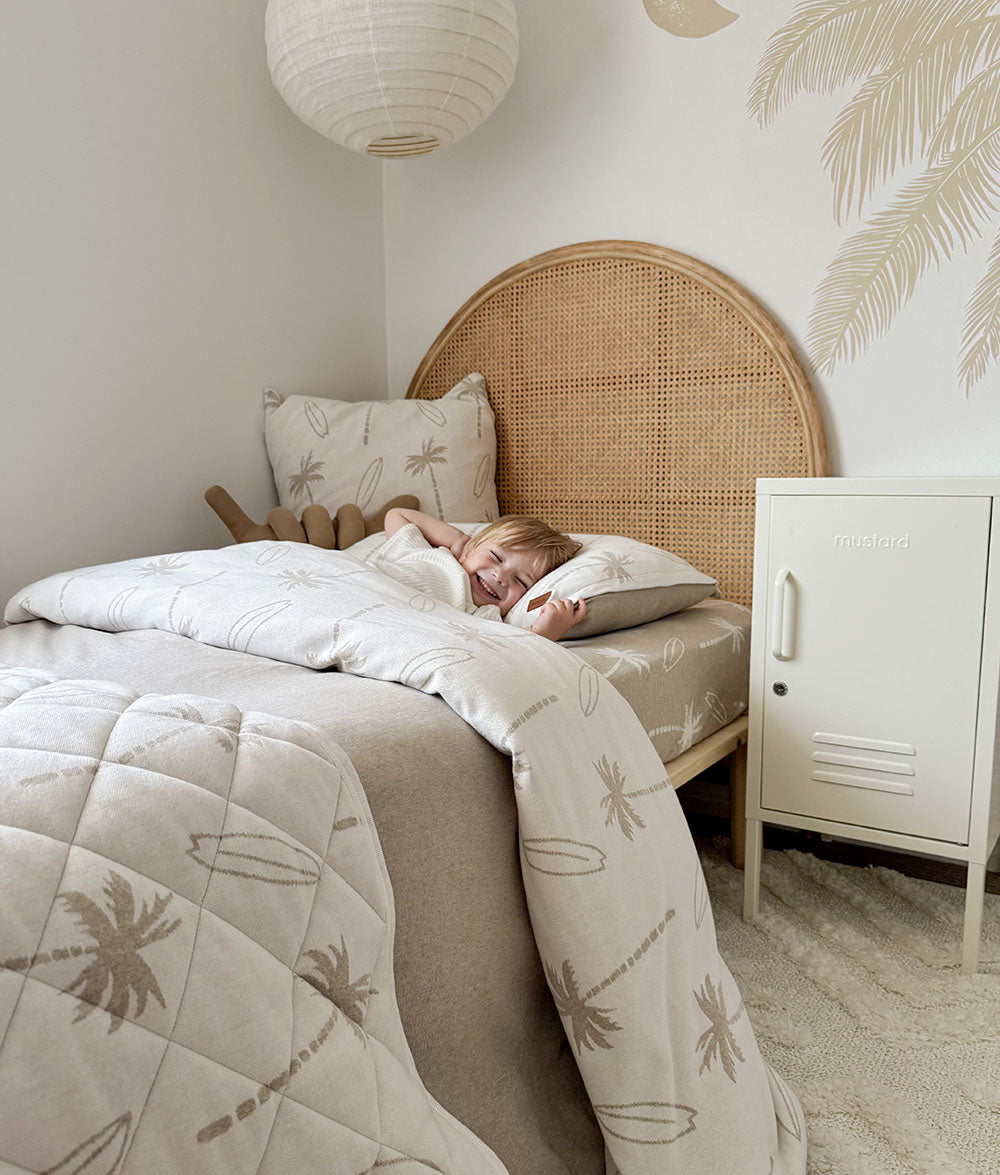 Person lying in bed with palm tree patterned bedding in a cozy bedroom.