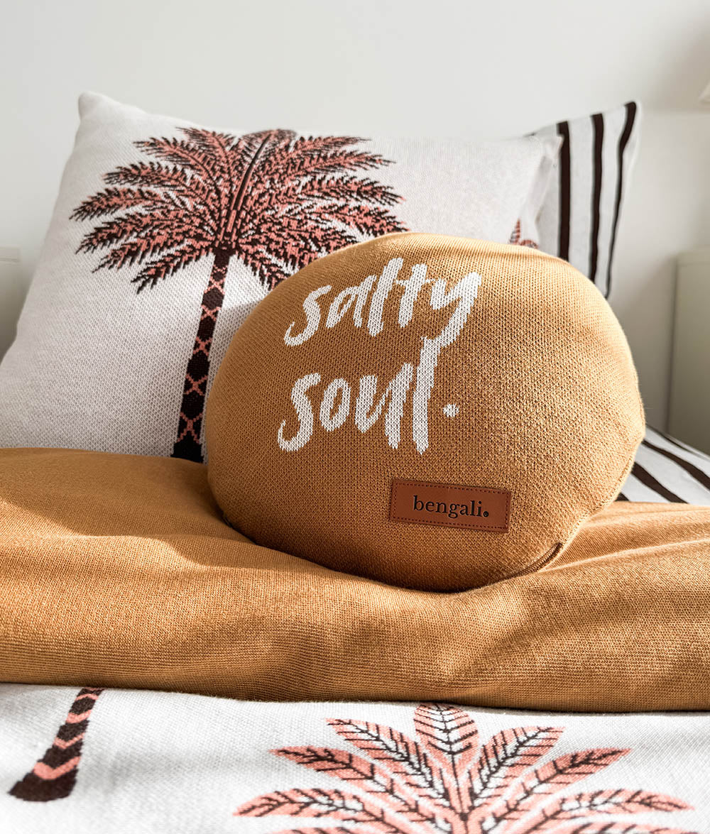 A round tan throw pillow with 'salty soul.' embroidered in white script and a small brown 'bengali' label.