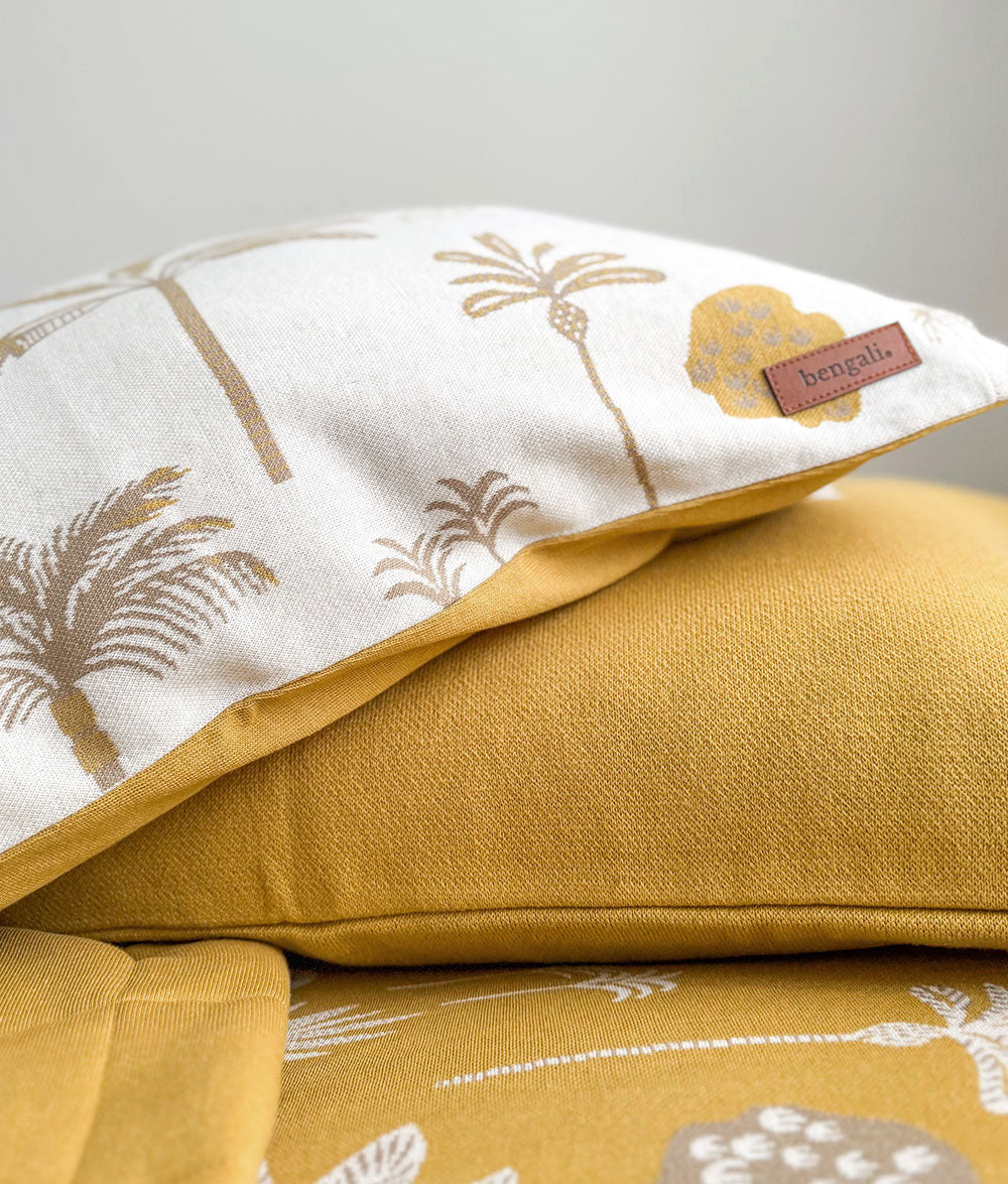 A close-up of a mustard yellow and white patterned bedding set, featuring a solid yellow pillow resting on a matching yellow and white tropical print duvet or comforter. A small brown fabric brand label reading 'bengali' is visible on the white pillow.