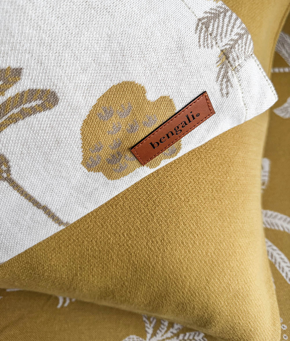 A close-up of a Bengali brand pillowcase on mustard yellow pillowcase with a white patterned top section and a brown leather brand label.