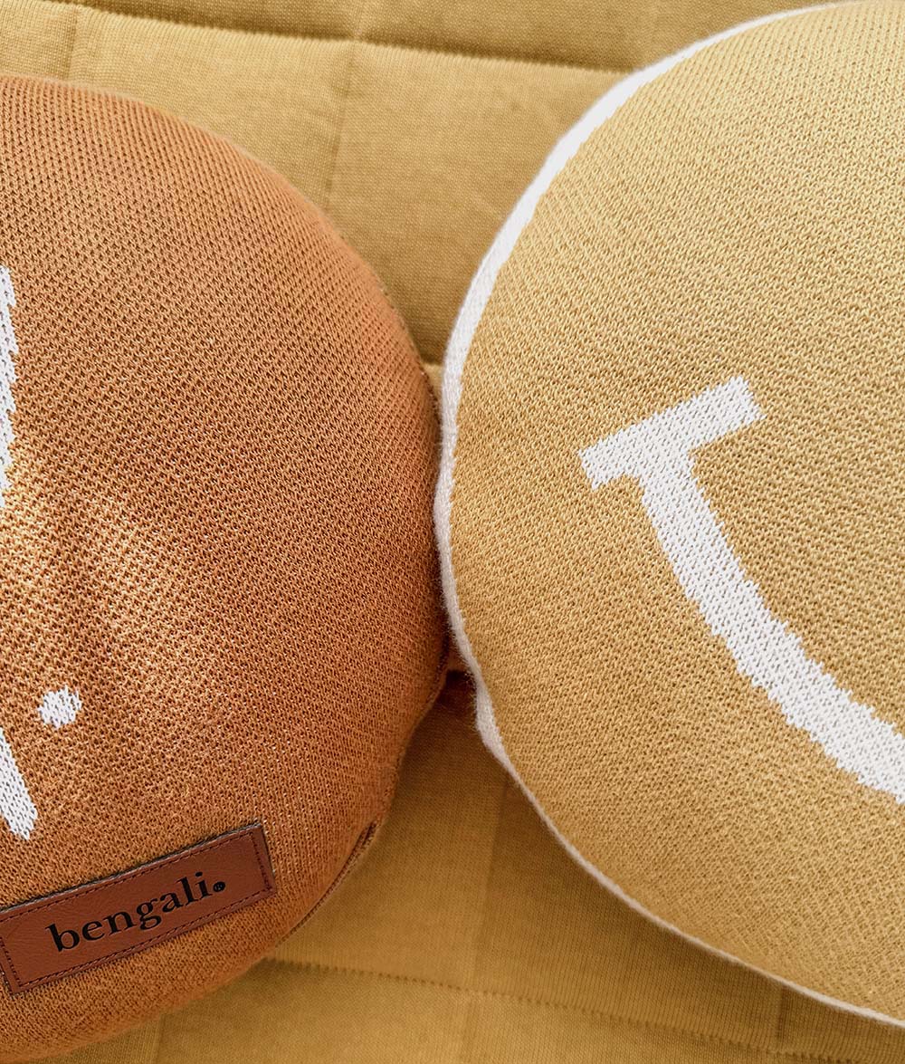 Close-up of the Salty Soul knitted cushion and Smiley knitted cushion styled side by side on matching mustard bedding.