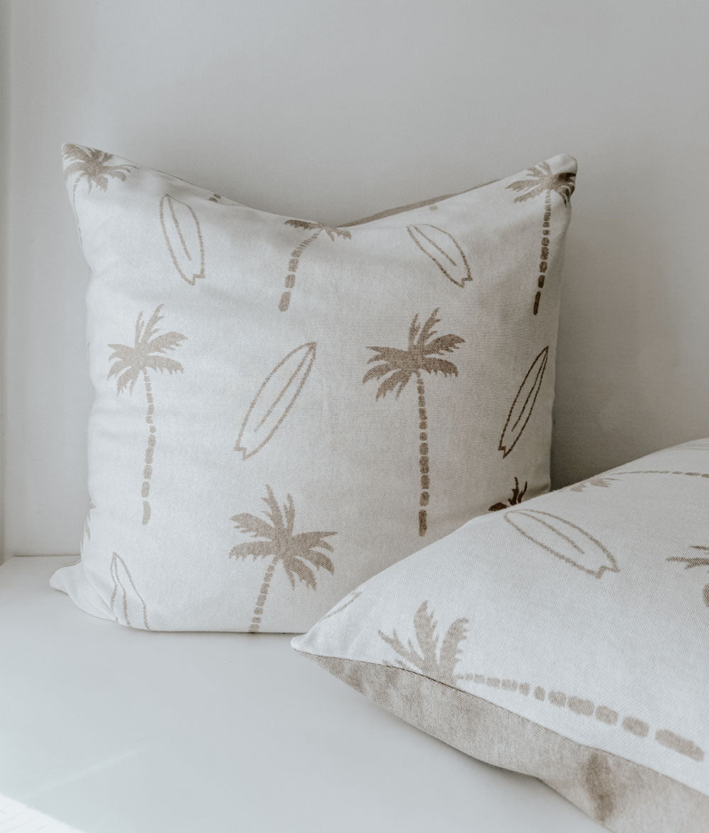 Decorative pillows with palm tree and surfboard pattern on a neutral background