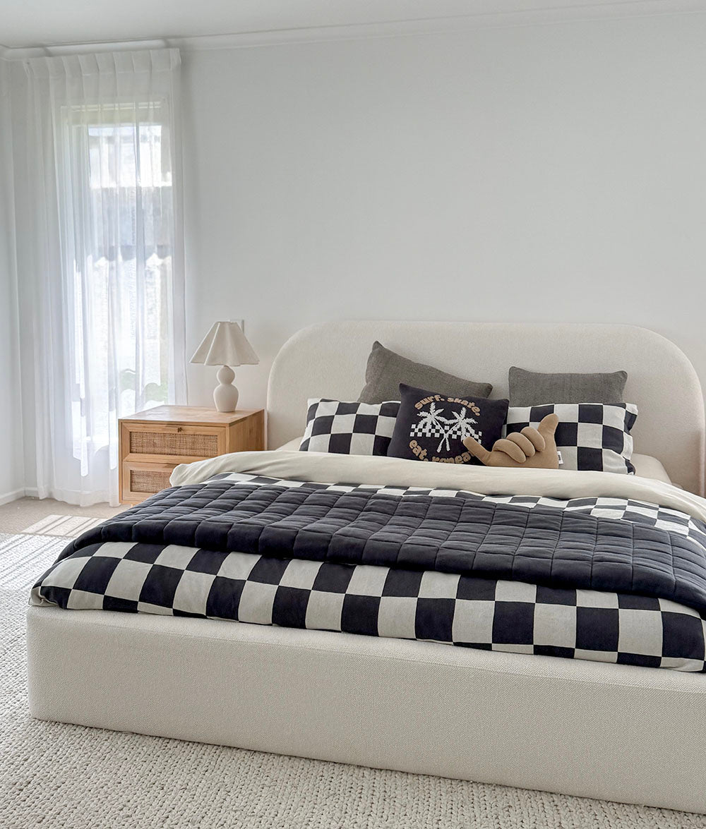 Bedroom with a bed featuring a checkered quilt and pillows, next to a nightstand with a lamp.