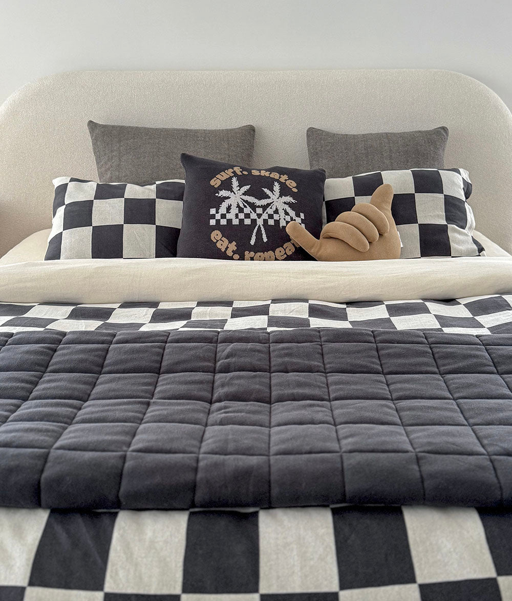 Bed with checkered bedding and decorative pillows against a white wall