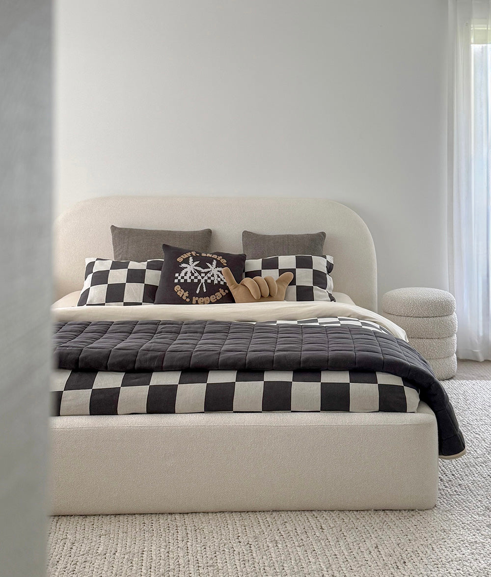 Beige upholstered bed with checkered blanket and pillows in a minimalistic room.