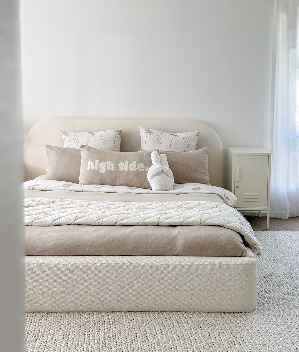 Neatly made bed with decorative pillows and a blanket in a minimalistic bedroom.