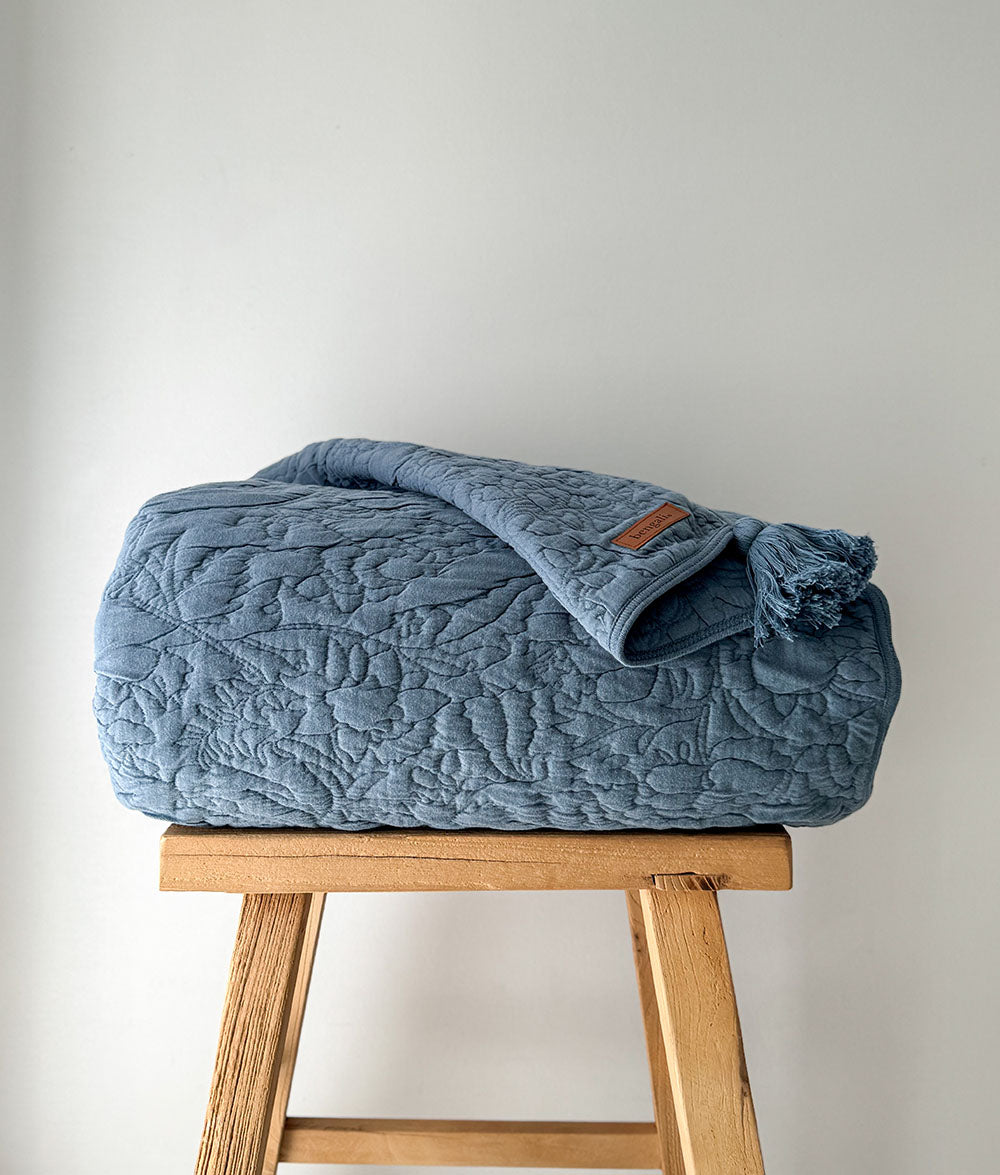 Blue textured blanket on a wooden stool against a light gray background
