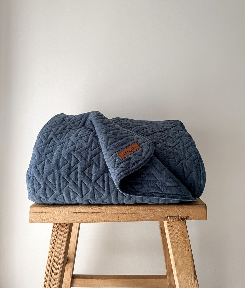 Blue quilted blanket on a wooden stool against a plain background