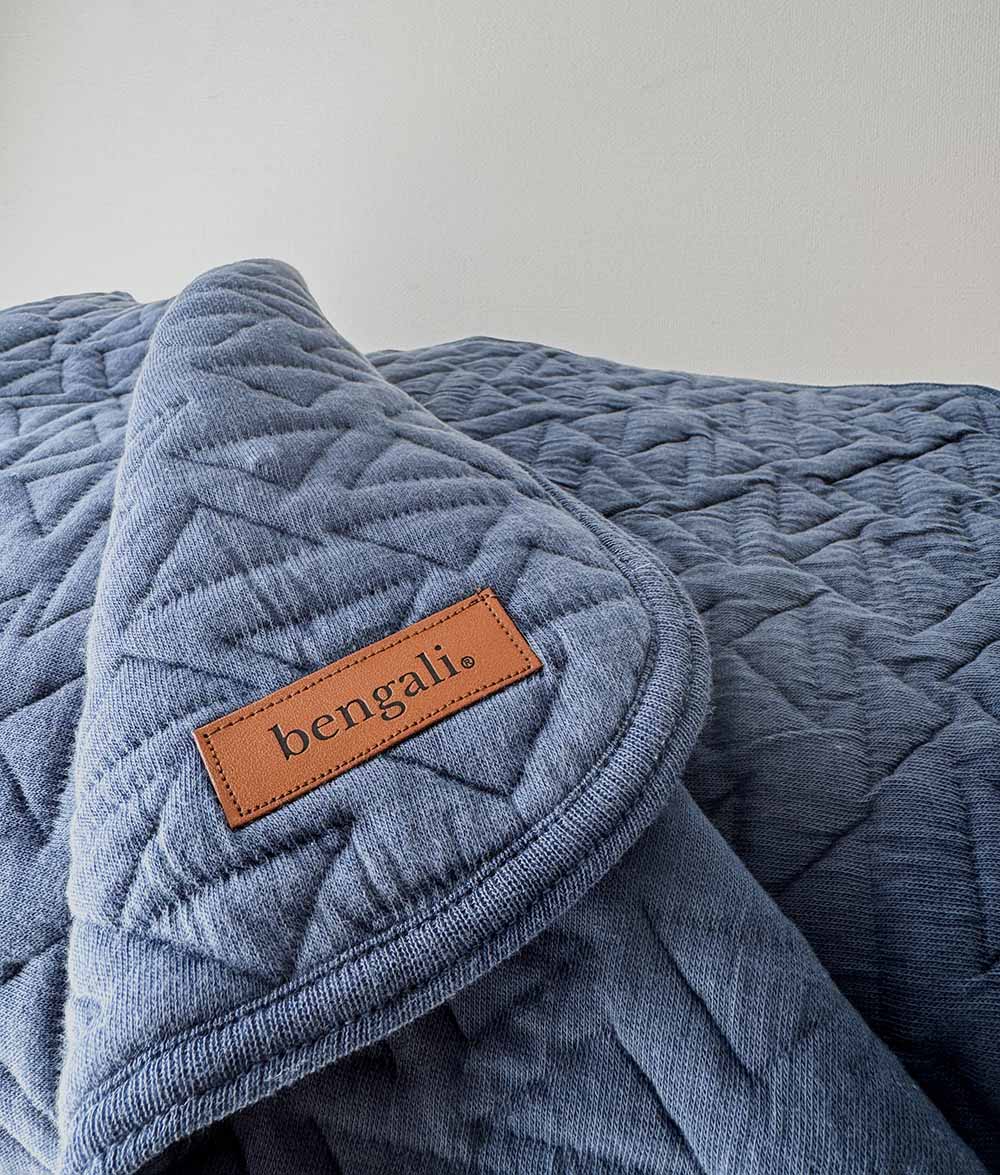 Blue quilted blanket with a 'bengali' label on a light gray background