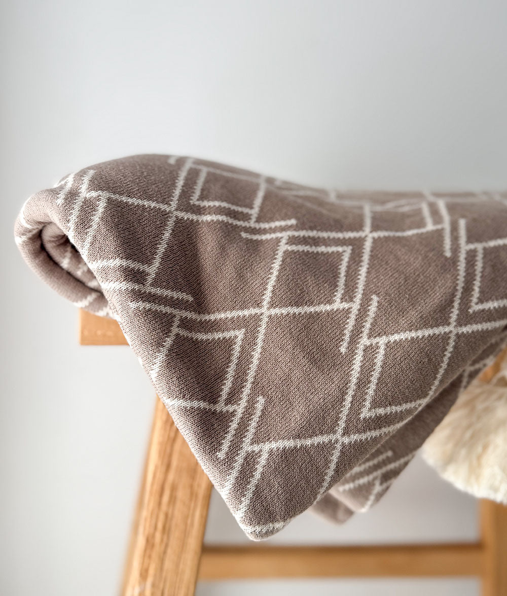 Brown blanket with geometric pattern draped over a wooden chair against a light background