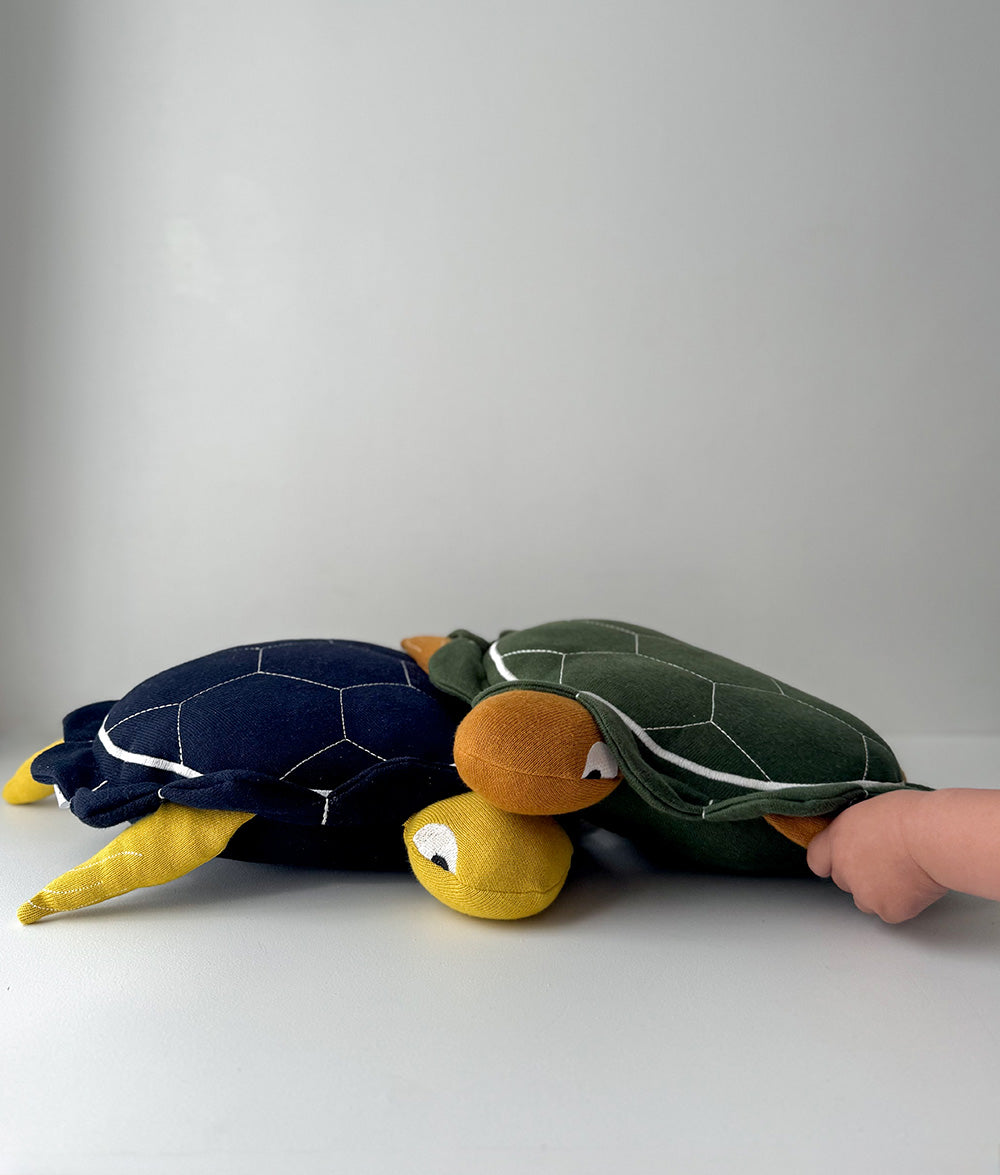 Two plush turtle toys, one navy and one green, on a white surface with a gray background.