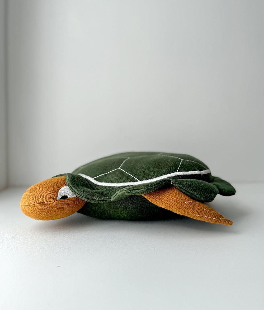 Plush turtle toy on a white surface with a light gray background