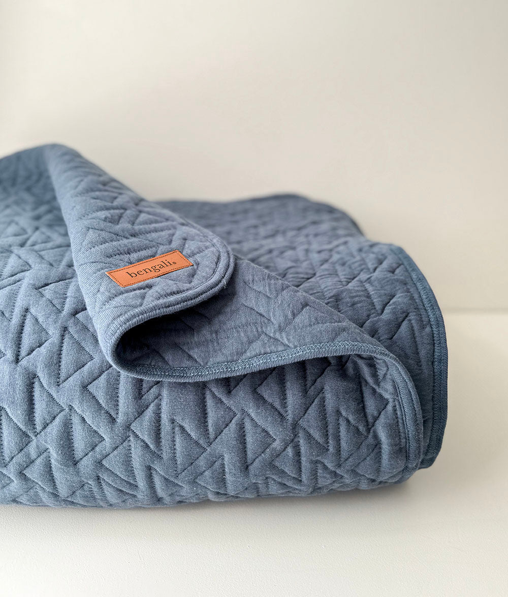 Quilted blue blanket with a brand label on a light background