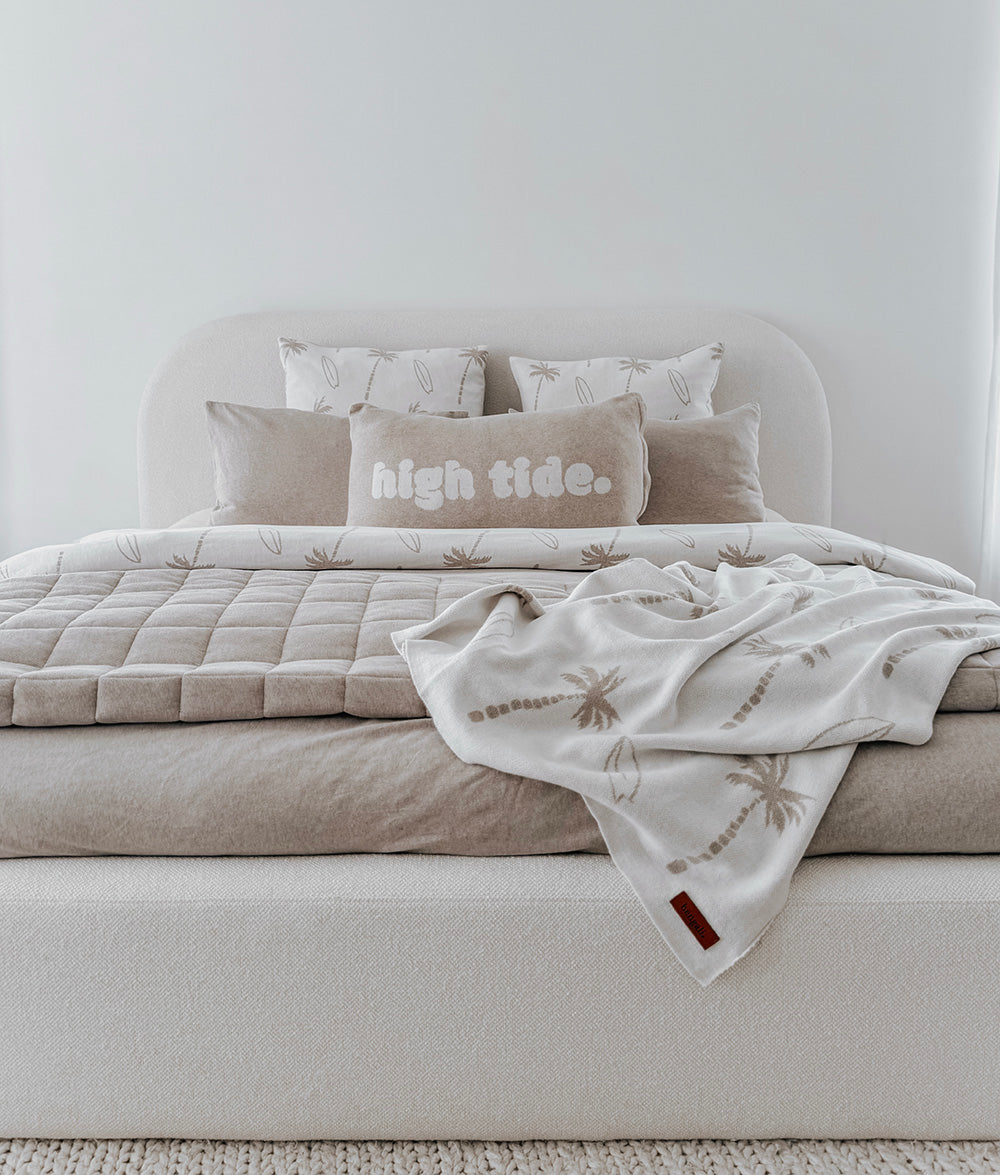 Neatly made bed with beige bedding and decorative pillows in a minimalistic room.