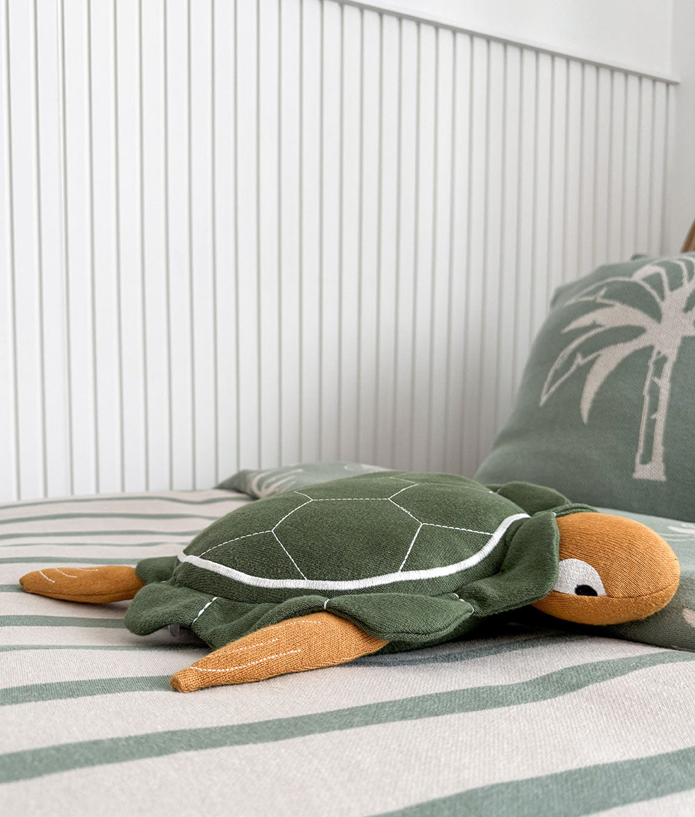 Green turtle-shaped pillow on a bed with striped bedding