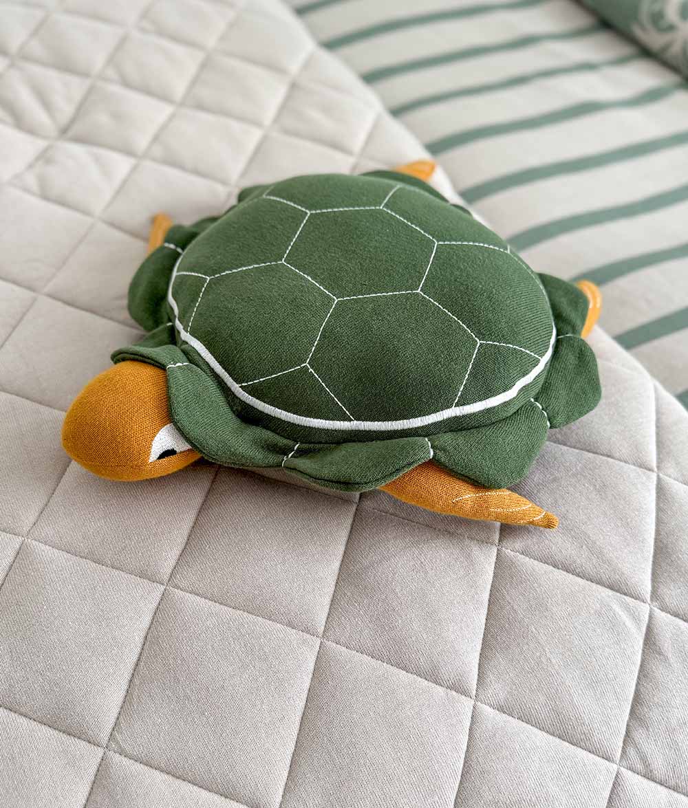 Green plush turtle toy on a quilted surface with striped fabric in the background