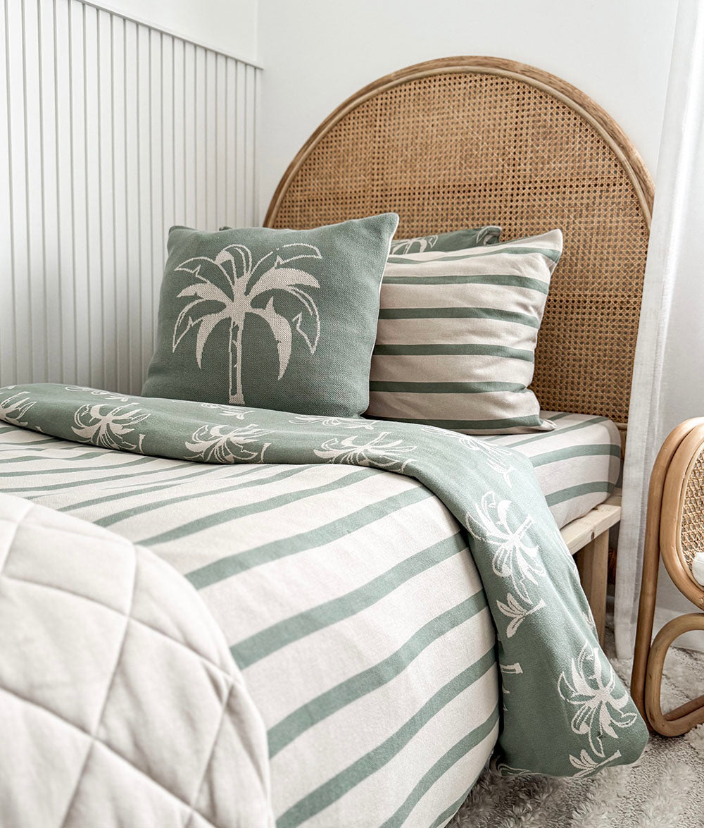 Bed with green and white striped bedding and palm tree design, against a white wall.