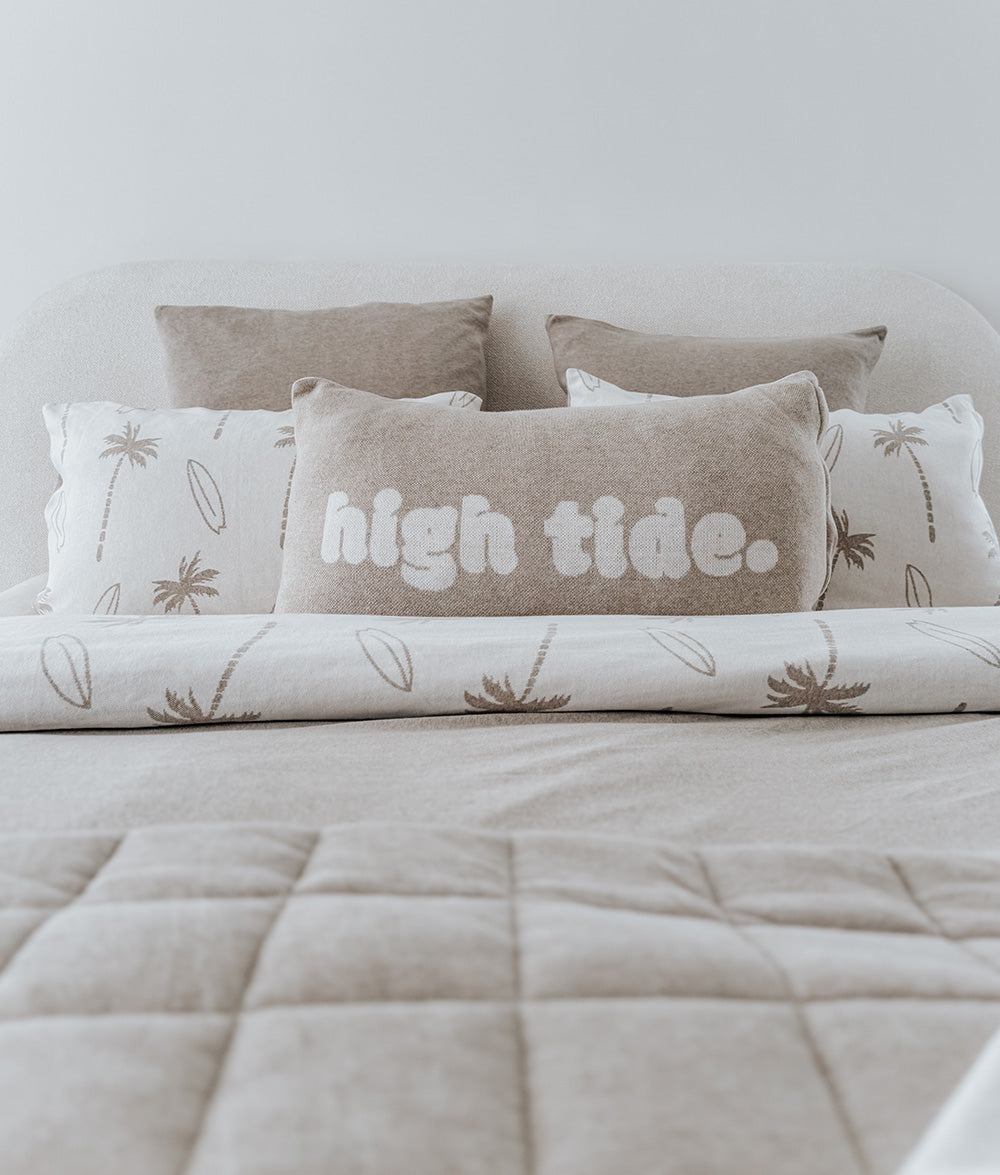 Bed with decorative pillows featuring 'high tide.' text and leaf patterns.
