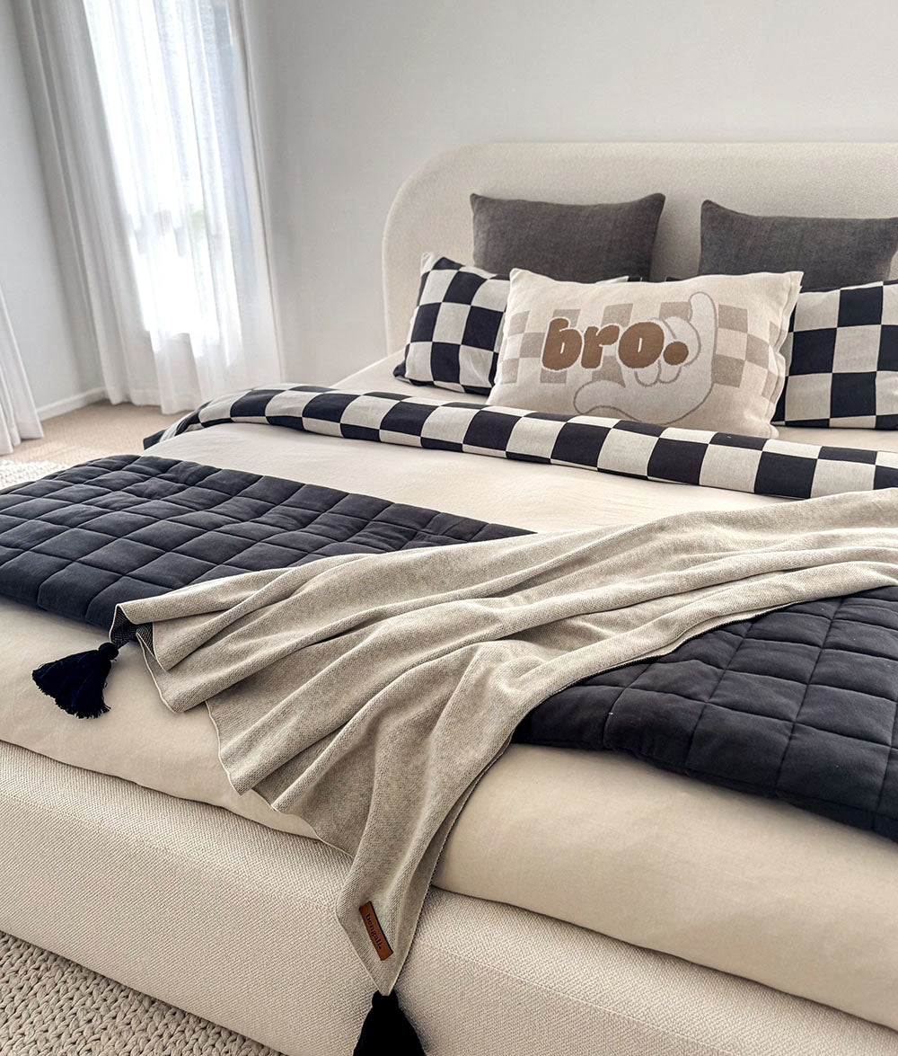 Neatly made bed with checkered and solid pillows, a blanket, and a feature 'bro' pillow.