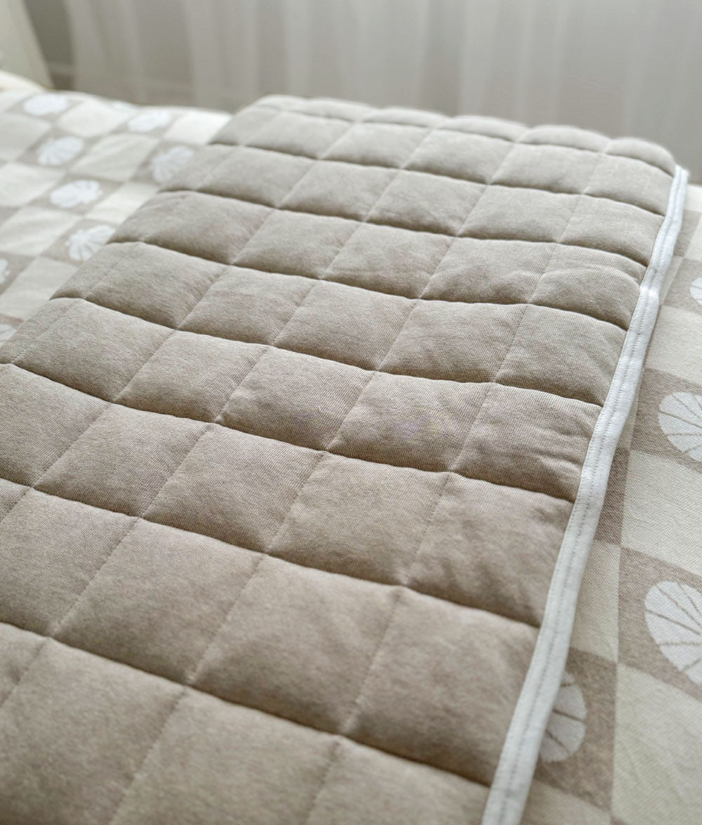 Beige quilted mattress pad on a bed with a light background