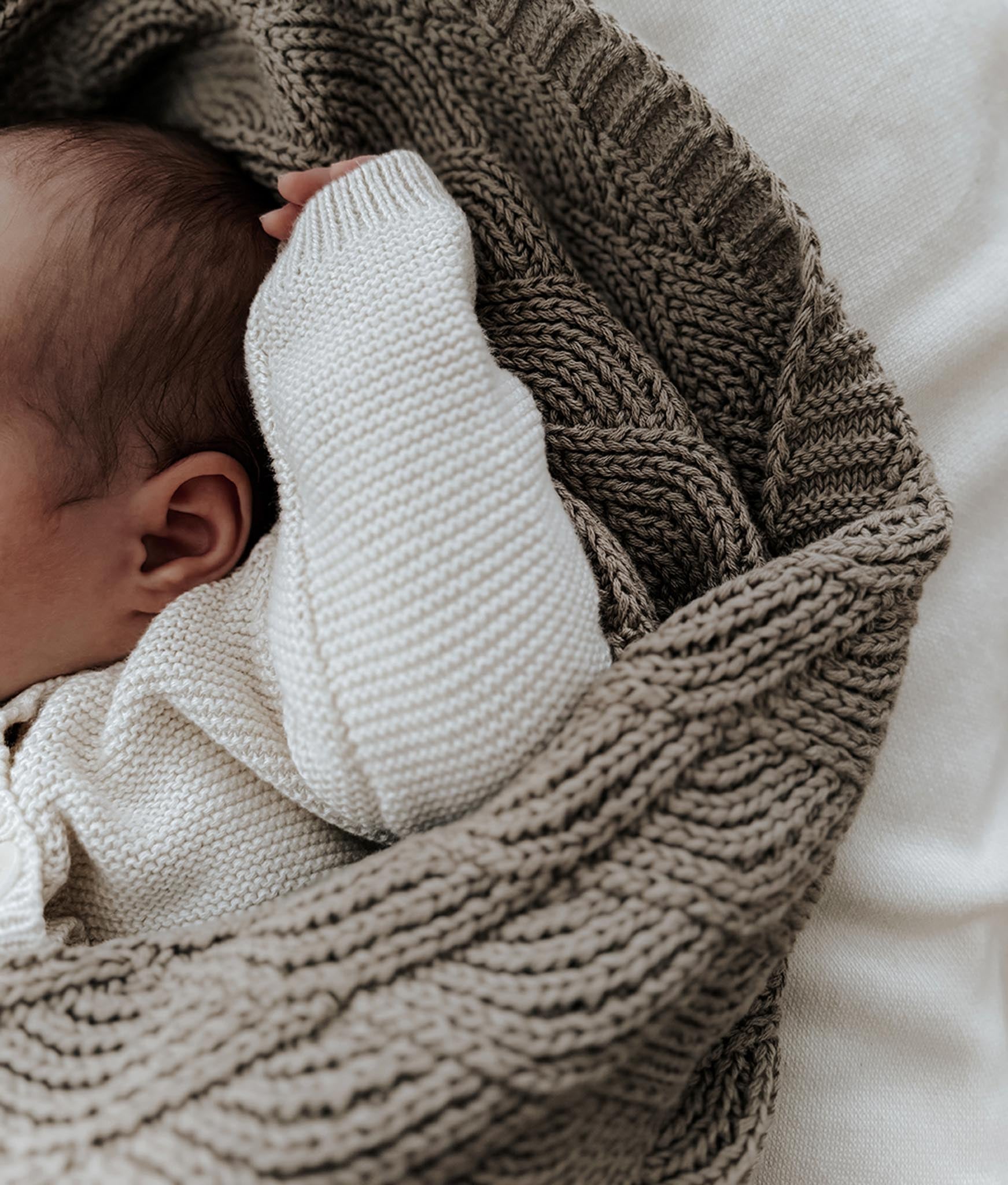 Baby wrapped in a textured brown blanket with a neutral background