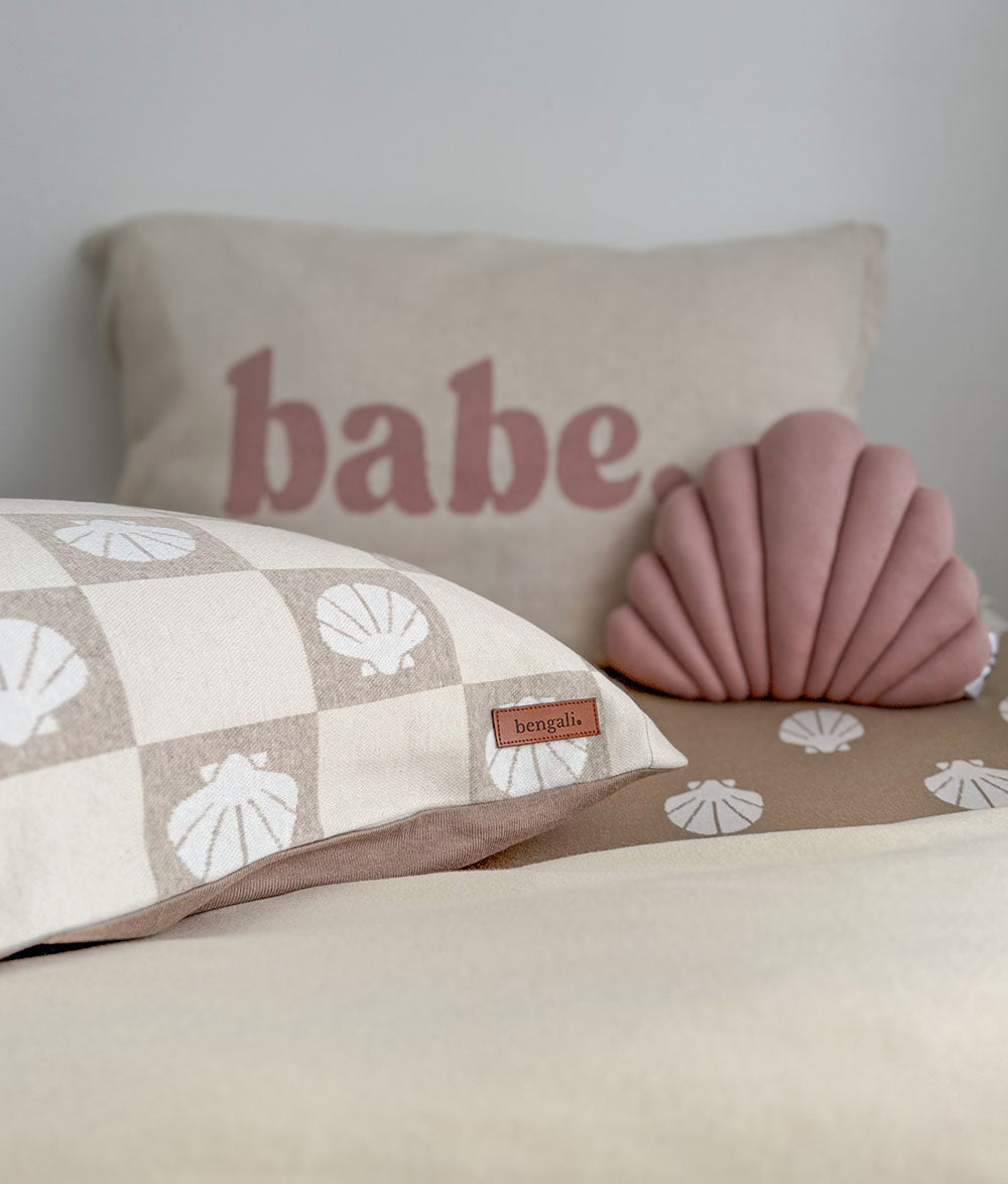 Decorative pillows with 'babe' text and shell pattern on a bed.
