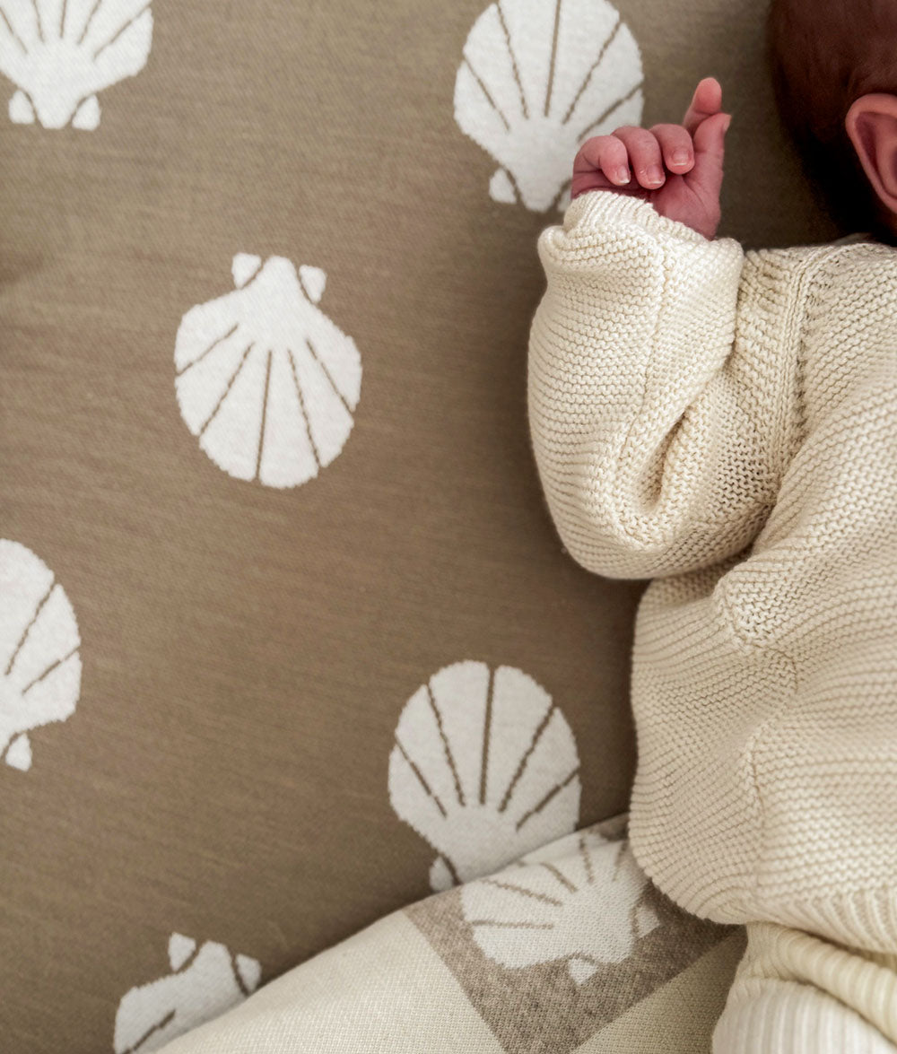 Baby in a beige sweater against a brown fabric background with shell patterns